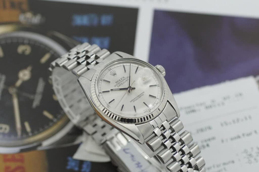 Rolex Datejust occasion vintage à lunette cannelée et bracelet Jubilee sur fond de documents horlogers.