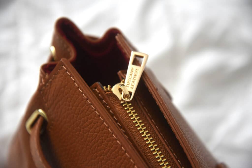 Gros plan sur la fermeture éclair dorée et les coutures d’un sac en cuir marron