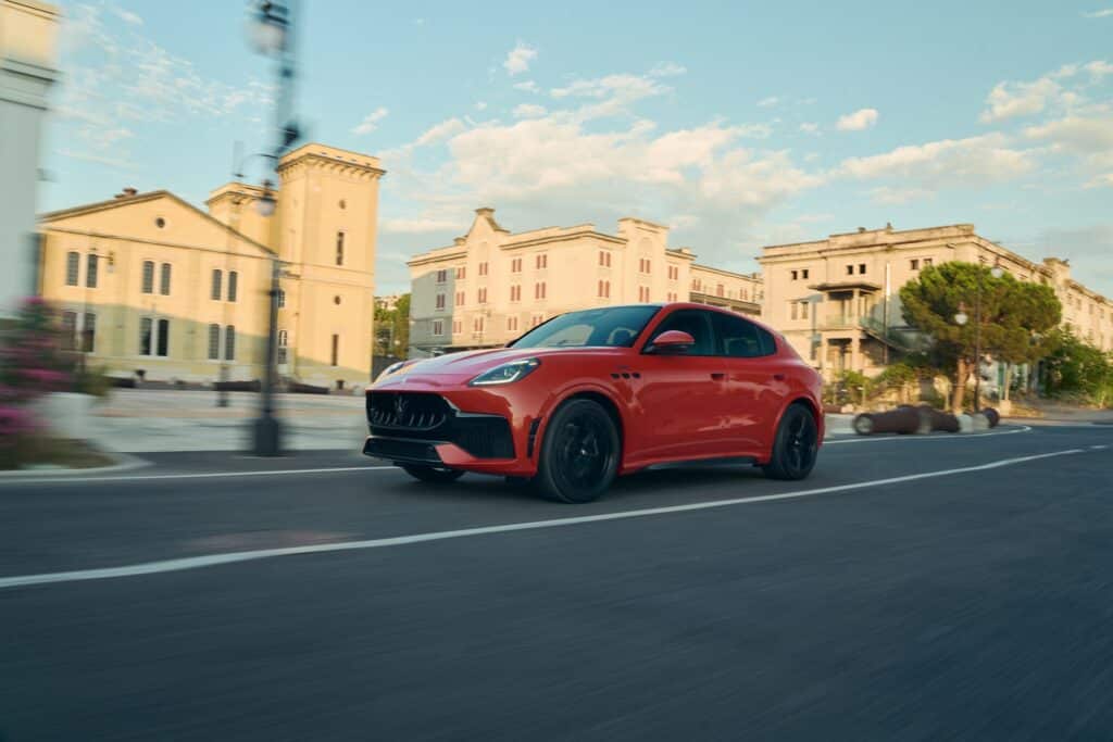 Les 10 SUV de luxe les plus sportifs en 2026 : Maserati Grecale Trofeo orange à toit noir vue de trois-quarts avant en mouvement dans une rue ensoleillée
