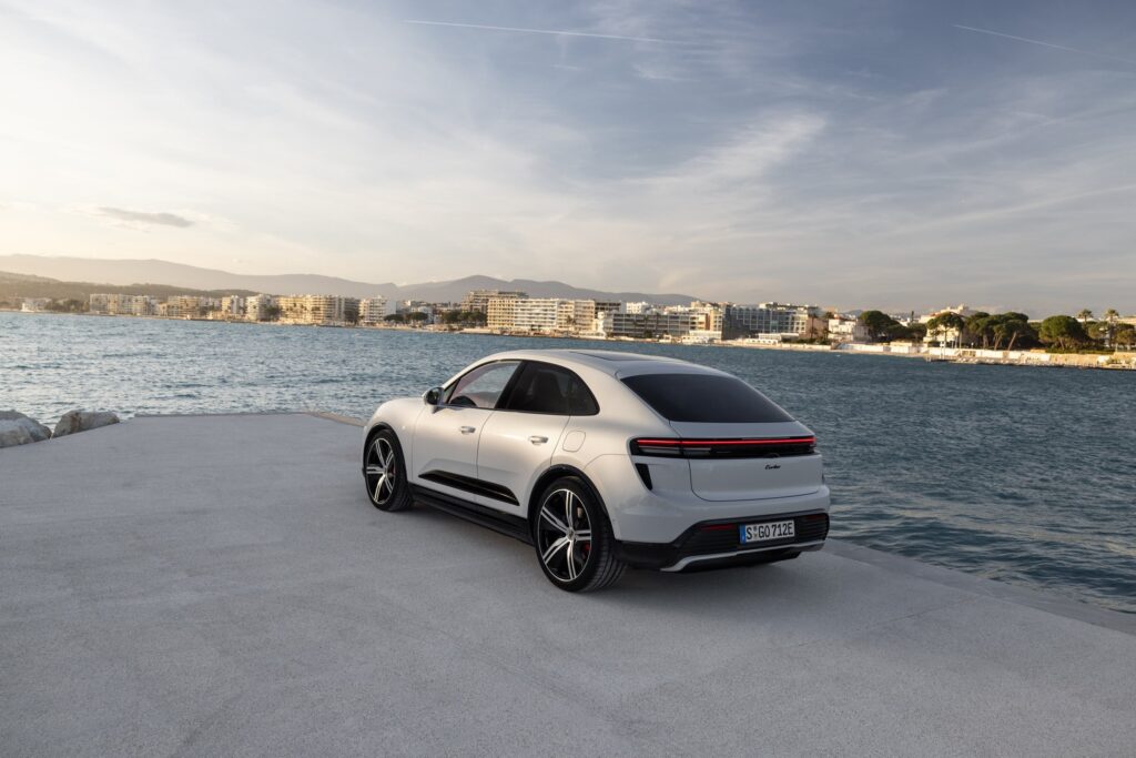 Les 10 SUV de luxe les plus sportifs en 2026 : Porsche Macan Turbo électrique gris Ice Grey vu de trois-quarts arrière face à la mer, bandeau lumineux arrière