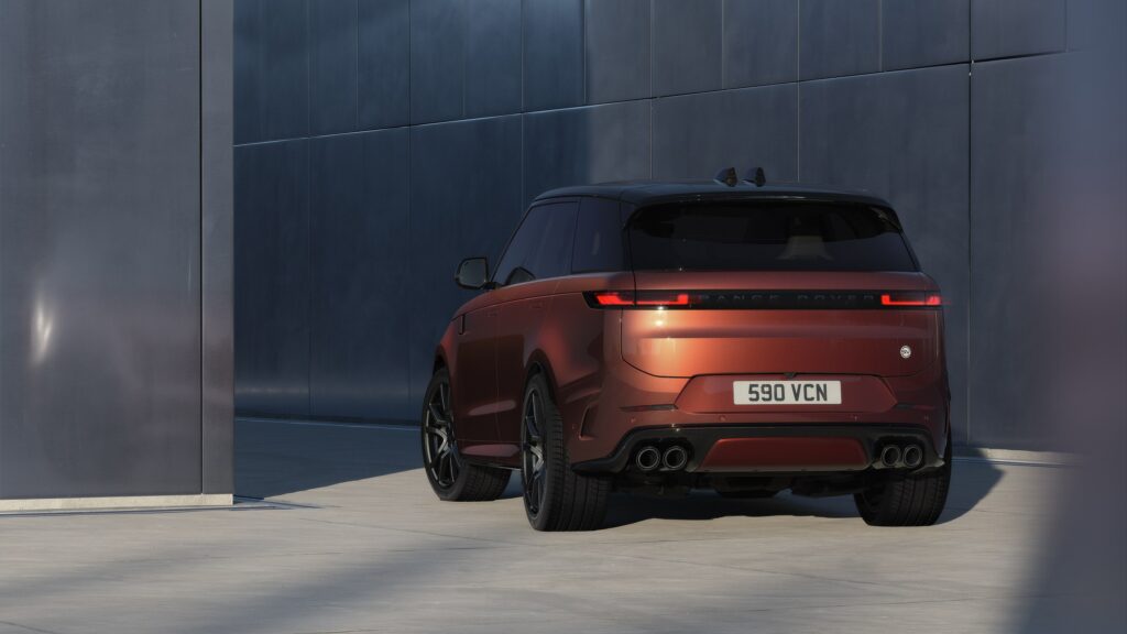 Range Rover Sport SV Carbon cuivré vu de trois-quarts arrière devant une façade de métal, quatre sorties d'échappement