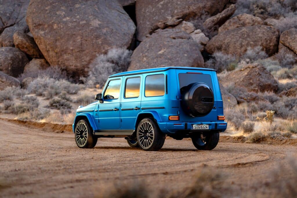 Mercedes-AMG G 63 bleu mat vu de trois-quarts arrière sur une piste désertique, roue de secours noire