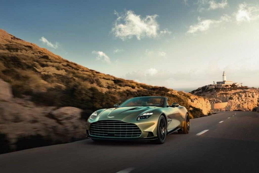 Les 10 Aston Martin les plus désirables en 2026 : Aston Martin Vanquish Volante vert décapotée sur une route côtière, vue de trois-quarts avant