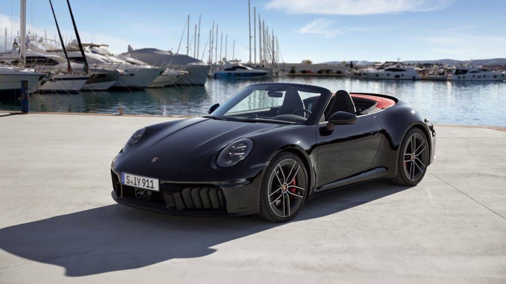Les 10 cabriolets de luxe les plus désirables en 2026 : Porsche 911 Carrera GTS Cabriolet noire capote ouverte sur un quai de port, vue de trois-quarts avant