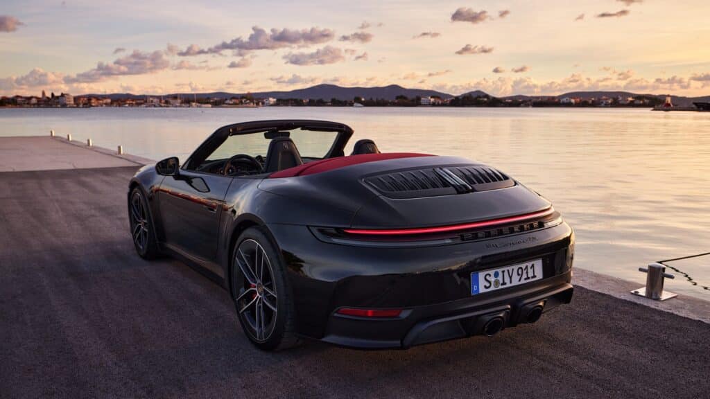 Porsche 911 Carrera GTS Cabriolet noire capote ouverte au bord de l'eau au coucher du soleil, vue de trois-quarts arrière