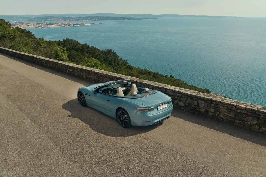 Maserati GranCabrio Folgore bleu clair décapotée sur une corniche au-dessus de la mer, vue de trois-quarts arrière