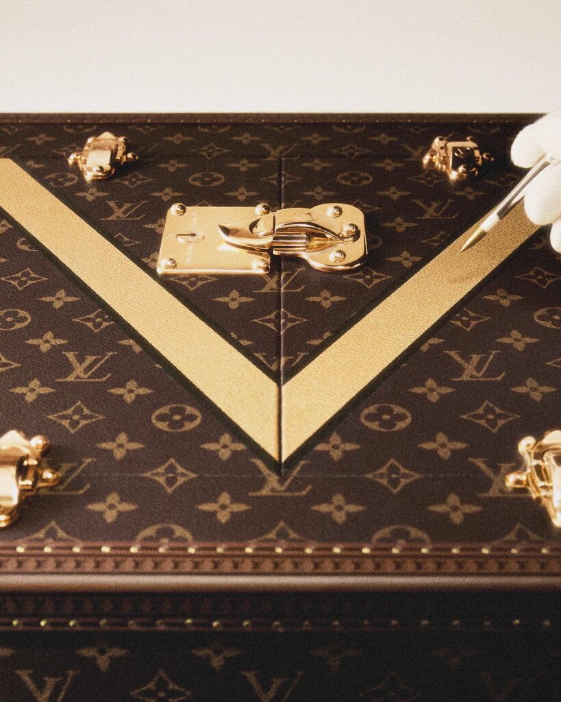 Mains gantées de blanc posant une charnière en laiton sur une malle Monogram Louis Vuitton