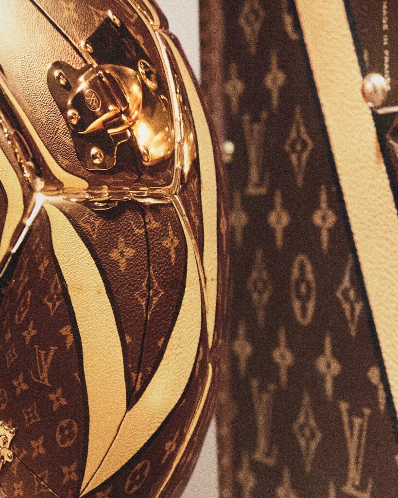 Gros plan granuleux sur la toile Monogram, une bande claire et une serrure en laiton d’une malle Louis Vuitton